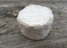 A photo of a White Nancy goat's cheese. It is positioned on a rustic, wooden table