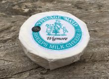 A picture of a wrapped wheel of Wigmore Cheese. It has been placed on a rustic wooden table.