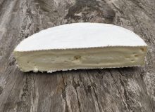 A picture of half a wheel of Wigmore Cheese. Is it positioned on a rustic wooden table