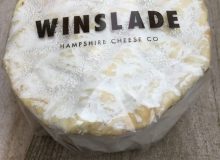 A photo of a whole little Winslade Cheese. It is positioned on a wooden board