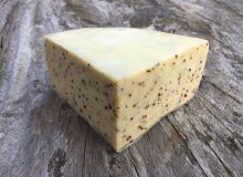 A picture of a wedge of Y-Fenni Cheese. It has a cream colour waxed rind and is positioned on a rustic wooden table